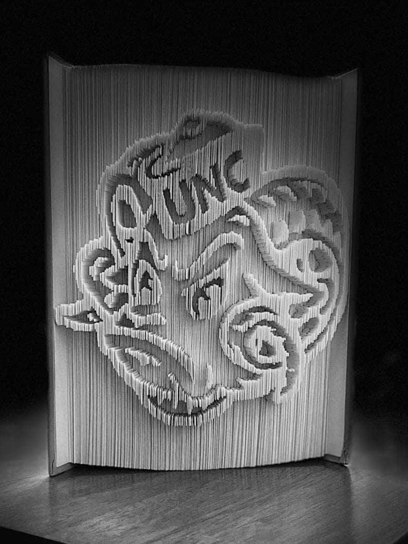 May include: A black and white book art sculpture of a stylized dragon with intricate details. The sculpture is made by folding pages of a book.