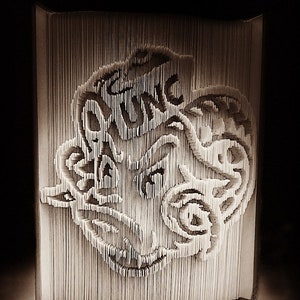 May include: A 3D paper art sculpture of a dragon's head, created by folding pages of a book. The dragon's head is made of white paper and has a detailed design.