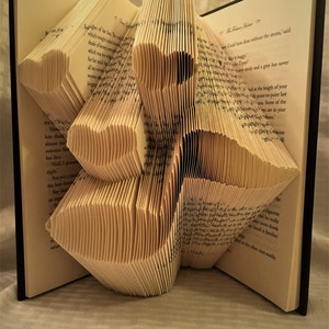 May include: A book folded into a three-dimensional origami-style sculpture of a flower. The book is open and the pages are folded to create the shape of the flower.
