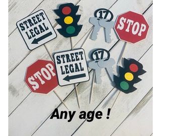 Puede incluir: Un conjunto de seis adornos para pasteles que incluyen una señal de alto, un semáforo, una llave y una señal que dice "Street Legal". Las señales son blancas con texto negro y el semáforo es rojo, amarillo y verde. La llave es plateada y la señal de alto es roja con texto blanco.