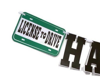 May include: A green and white license plate-shaped banner with the text "LICENSE TO DRIVE" in bold black letters. A black and white banner with the letters "HA" is attached. The background is white.