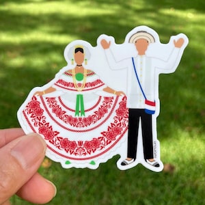 May include: A sticker featuring a couple in traditional Colombian clothing. The woman wears a white dress with red and green embroidery, and the man wears a white shirt, black pants, and a straw hat.