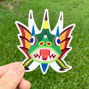 May include: A sticker of a green, red, yellow, and blue cartoon fish with a toothy grin. The fish has a large, open mouth with sharp teeth and a red tongue. The fish has a yellow and red fin on each side of its head. The sticker is on a white background.