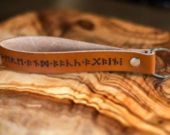 May include: Brown leather keychain with a silver key ring. The leather strap has black runes engraved on it.