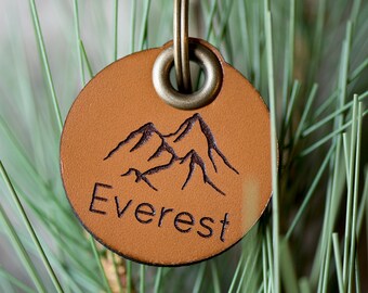 Peut inclure: Un porte-clés en cuir marron avec une silhouette de montagne et le mot "Everest" gravé dessus. Le porte-clés est attaché à un anneau de clé en laiton.