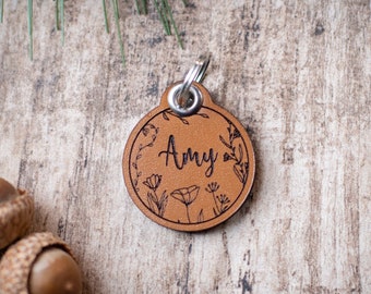 May include: A brown leather dog tag with a floral design and the name "Amy" engraved on it.