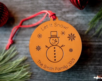 May include: A brown leather Christmas ornament with a snowman design and the text "Let it Snow! The Smith Family 2021".