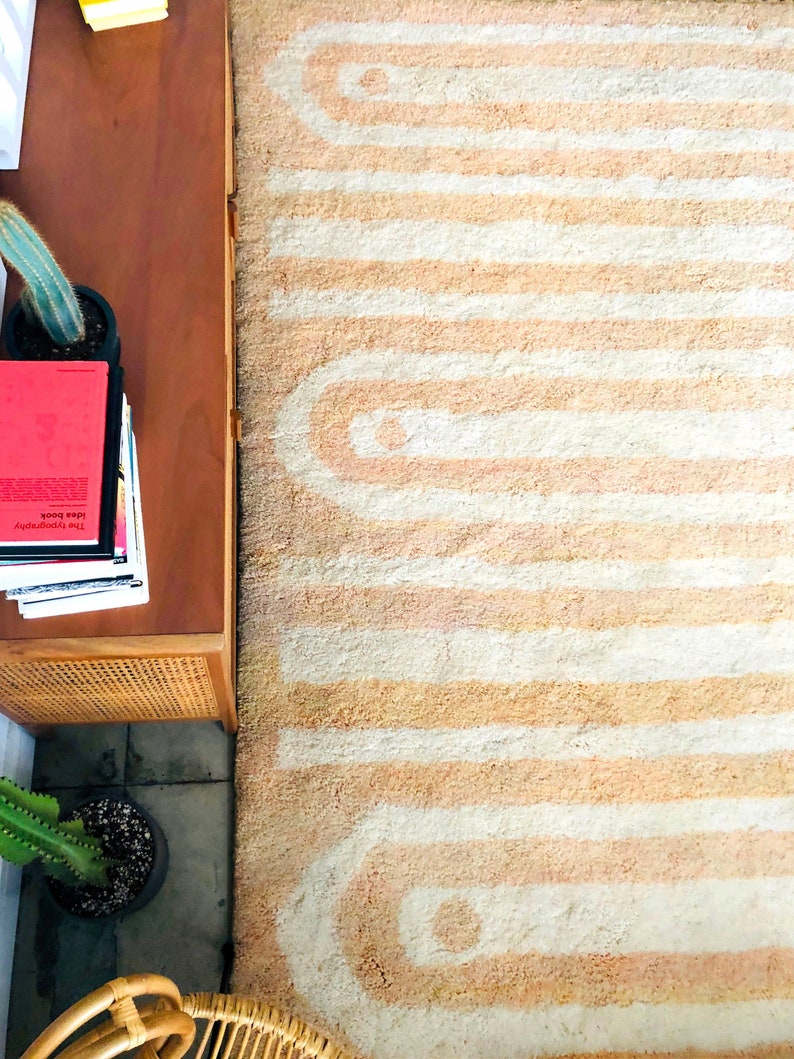 May include: A light pink and white rug with a geometric pattern. The rug has a fuzzy texture and is made of a soft material.