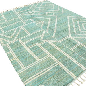 May include: A teal and white geometric patterned rug with a fringe border.