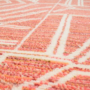 Puede incluir: Primer plano de una alfombra de color rosa y blanco con un dise&ntilde;o geom&eacute;trico. La alfombra est&aacute; hecha de un material suave y esponjoso.
