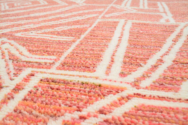 Puede incluir: Primer plano de una alfombra de color rosa y blanco con un dise&ntilde;o geom&eacute;trico. La alfombra est&aacute; hecha de un material suave y esponjoso.