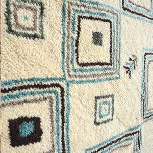 May include: A white rug with a geometric pattern of squares in shades of blue, brown, and gray.