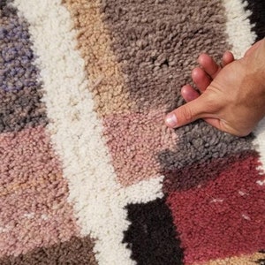 Puede incluir: Primer plano de una alfombra colorida y multitexturada con una mano descansando sobre la superficie. La alfombra presenta una variedad de colores, incluyendo rosa, marr&oacute;n, blanco y negro.