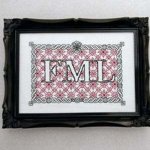 May include: A black framed embroidery with a red and white pattern and the text "FML" in white.