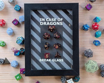 May include: A black framed shadow box with the text "IN CASE OF DRAGONS BREAK GLASS" and a collection of colorful dice inside.