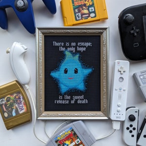 May include: A framed cross-stitch featuring a blue star character and the text "There is no escape; the only hope is the sweet release of death". The frame is silver with a black background. The image is surrounded by various Nintendo game cartridges and controllers.