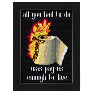 Op de afbeelding: Kruissteekkunst in een zwarte lijst. Het ontwerp toont een gepixeleerde haan met vlammen en de tekst "all you had to do was pay us enough to live" in het wit.
