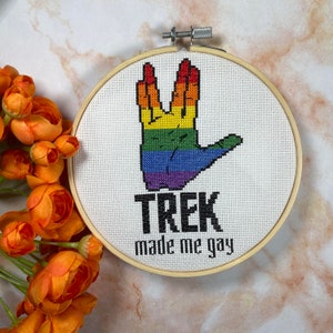 May include: A white embroidery hoop with a rainbow colored Star Trek Vulcan salute hand and the text "TREK made me gay".