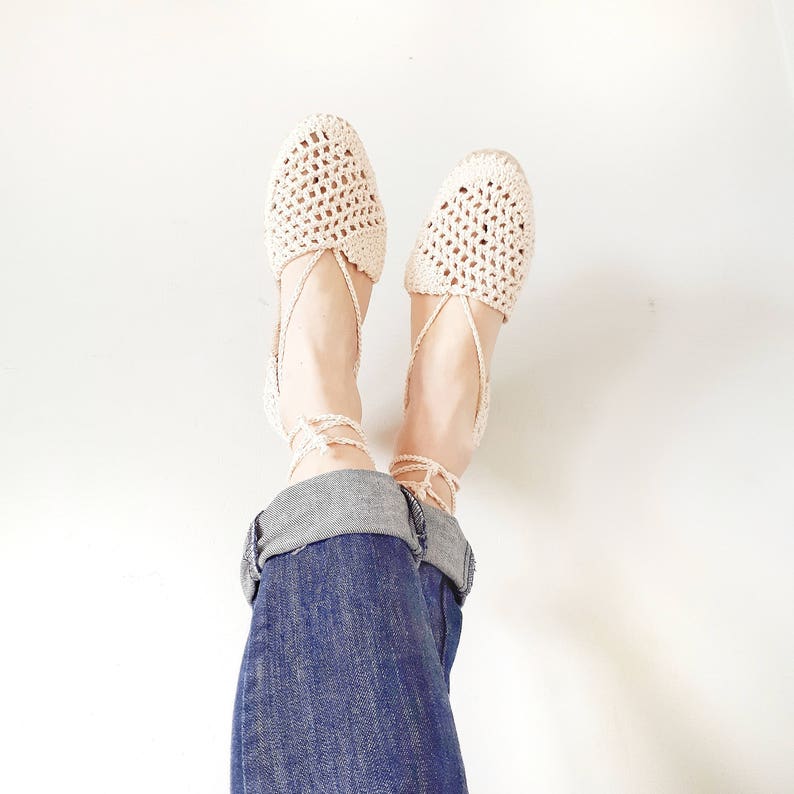 May include: A pair of white crocheted espadrille sandals with ankle ties. The sandals are worn with blue jeans.