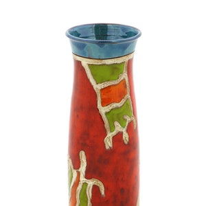 Könnte beinhalten: Eine rote Keramikvase mit blauem Rand und einem geometrischen Muster in Grün, Orange und Weiß.