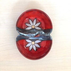 May include: A red ceramic double dish with a blue glaze and white flower designs. The dish is divided into two sections.