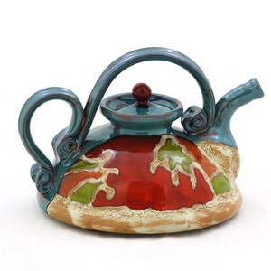 Könnte beinhalten: Eine türkise Keramik-Teekanne mit roter und grüner Glasur. Die Teekanne hat eine einzigartige, abgerundete Form und einen Deckel mit einem kleinen Knopf.