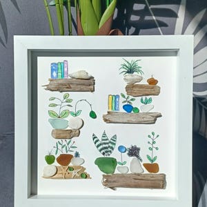 May include: A framed artwork made with sea glass and driftwood, depicting a series of shelves with potted plants, books, and other decorative elements. The artwork is set against a white background.