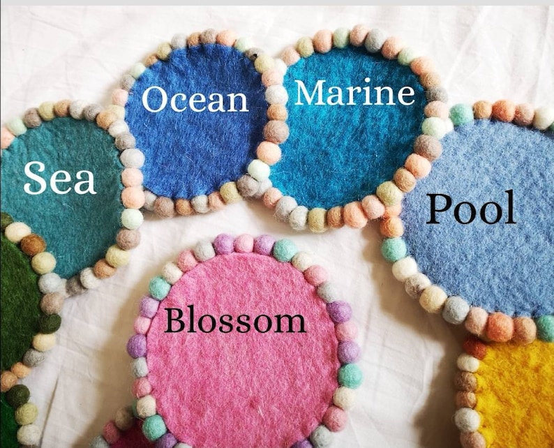 May include: Six colorful felt coasters with pom-pom trim. The coasters are labeled "Sea", "Ocean", "Marine", "Pool", "Blossom", and an unlabeled yellow coaster.