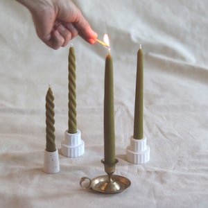May include: Three green candles on white holders, one is lit, and a gold metal candle holder with a green candle.