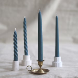 May include: Three teal candles on different holders. The candles are on a white surface. The candle on the left is twisted, the candle in the middle is straight, and the candle on the right is twisted.