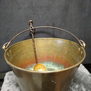 May include: A large, brass bucket with a handle and a matching ladle. The bucket has a worn, aged patina and is likely antique.