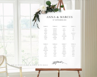 May include: A white wedding seating chart with black text on an easel. The chart lists the names of guests assigned to each table. The chart is titled "Anna & Marcus" and "18th September 2021".