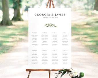 May include: A white seating chart with a green leafy branch design. The chart lists the names of guests for a wedding reception, with tables numbered 1 through 8. The chart is displayed on a wooden easel.