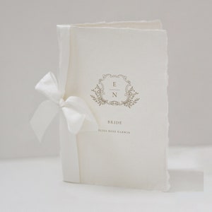 May include: A white wedding program with a decorative floral design and the initials "E & N" in a gold frame. The text "Bride" and "Elisa Rose Darwin" is printed below the design.