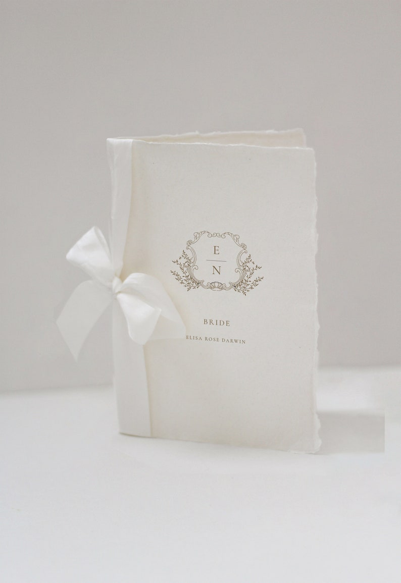 May include: A white wedding program with a decorative floral design and the initials "E & N" in a gold frame. The text "Bride" and "Elisa Rose Darwin" is printed below the design.