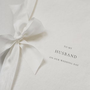 May include: A white card with a white ribbon tied in a bow. The card says "To my Husband on our wedding day" and "A & J Santorini" at the bottom.