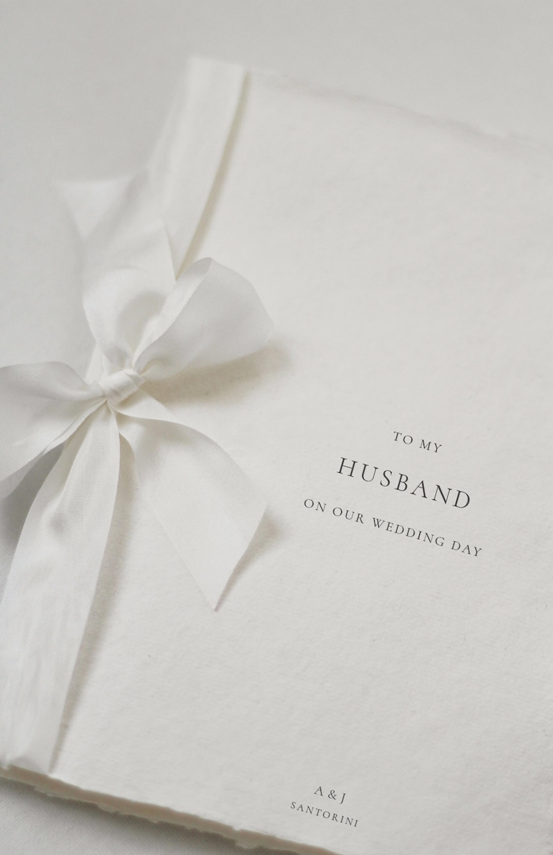 May include: A white card with a white ribbon tied in a bow. The card says "To my Husband on our wedding day" and "A & J Santorini" at the bottom.