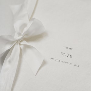 May include: A white card with a white ribbon tied in a bow. The card says "To My Wife On Our Wedding Day" and "A & J Santorini" at the bottom.