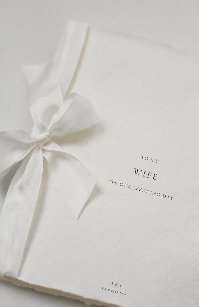 May include: A white card with a white ribbon tied in a bow. The card says "To My Wife On Our Wedding Day" and "A & J Santorini" at the bottom.