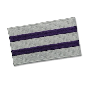 May include: A grey and purple striped fabric patch. The patch has two purple stripes on a grey background.