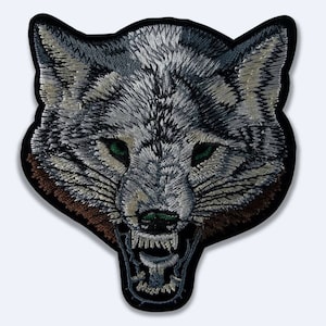 May include: Embroidered iron-on patch of a snarling wolf's head with a gray and white fur pattern, green eyes, and a brown muzzle.