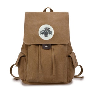 May include: A brown canvas backpack with a round sticker featuring a black and white stylized bird design. The backpack has a drawstring closure and two side pockets.