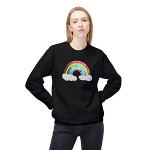 Peut inclure: Un sweat-shirt noir avec un motif arc-en-ciel en paillettes. L'arc-en-ciel a des nuages de chaque côté.
