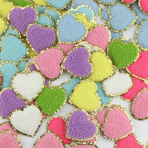 Peut inclure: Assortiment de patchs en forme de cœur en feutre de différentes couleurs avec une bordure dorée scintillante. Les cœurs sont de différentes couleurs, notamment rose, violet, bleu, vert et jaune.