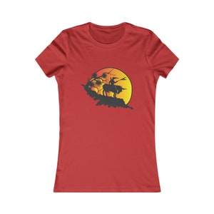 May include: A red women's t-shirt with a silhouette of a person riding a horse in front of a large orange and yellow sun.