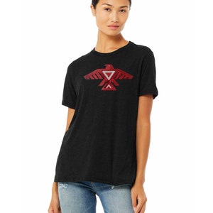 Peut inclure: Un t-shirt noir avec un motif d'aigle amérindien stylisé rouge sur le devant.
