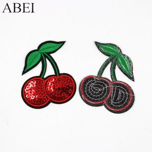 May include: Two embroidered iron-on patches of cherries. One patch features red sequins and the other is black with a silver outline.