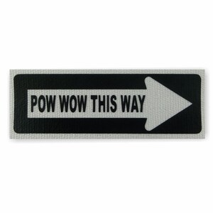 Peut inclure: Un panneau noir et blanc avec une flèche blanche pointant vers la droite. Le panneau indique "POW WOW THIS WAY".