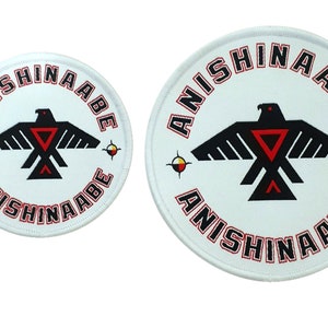 May include: Two white circular patches with red embroidered text "ANISHINAABE" around the edge. A black stylized bird with red accents is in the center of each patch. The smaller patch is on the left and the larger patch is on the right.