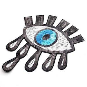 May include: A large, blue eye with white eyelashes and a white background. The eye is surrounded by six black teardrop shapes.